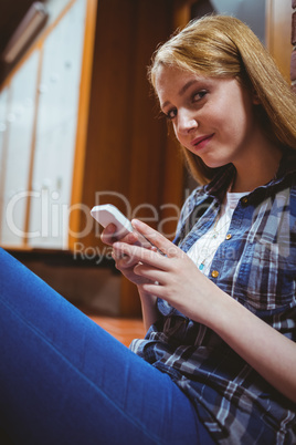 Pretty student sitting on the floor against the wall using smart