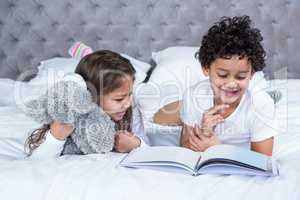 Cute sibling reading a book on the bed