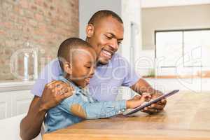 Cute son using tablet at desk with father