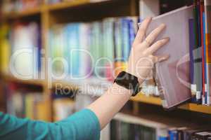 Students hand with smartwatch picking book from bookshelf