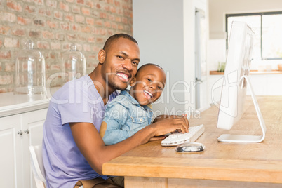 Cute son using laptop at desk with father