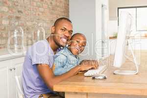 Cute son using laptop at desk with father