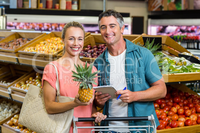 Smiling couple holding a pineapple and a grocery list