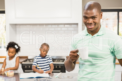 Father drinking hot beverage with children on background