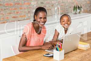 Cute daughter using laptop at desk with mother