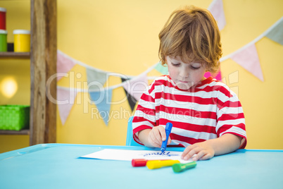 Smiling boy colouring some paper