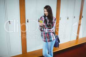 Cheerful student standing next the locker and using smartphone