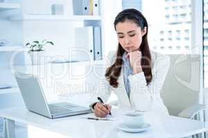 Thoughtful businesswoman writing on clipboard
