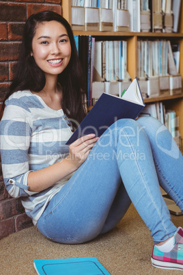 Smiling student sitting on the floor against wall in library rea