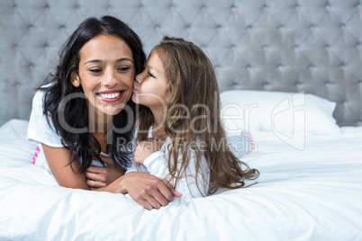 Cute child kissing her mother on the bed