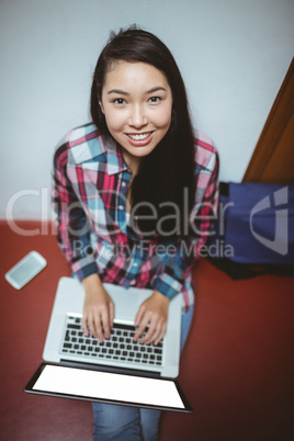 Smiling student sitting on the floor and using laptop