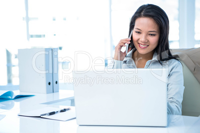 Smiling businesswoman on phone using laptop