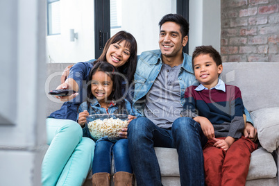 Happy young family eating popcorn while watching tv