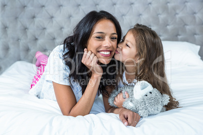 Cute child kissing her mother on the bed
