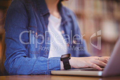 Student with smartwatch using laptop in library