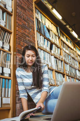 Smiling student sitting on the floor against wall in library stu