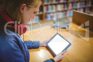 Pretty student with headphones using tablet in library