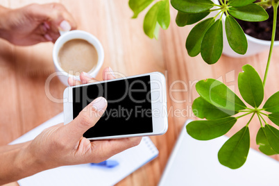 Overhead of feminine hands holding coffee and smartphone