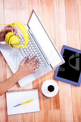 Overhead of feminine hands typing on laptop and holding headphon