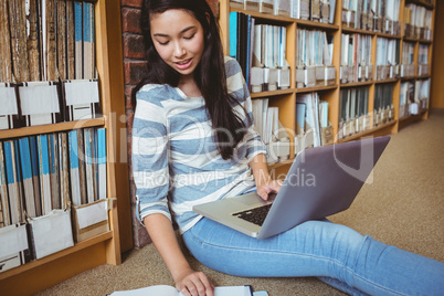 Smiling student sitting on the floor against wall in library stu