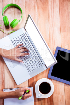 Overhead of feminine hand typing on laptop and taking notes