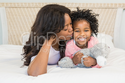 Mother kissing her smiling daughter on bed Mother kissing her smiling daughter on bed