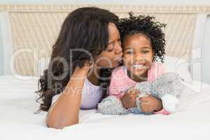 Mother kissing her smiling daughter on bed