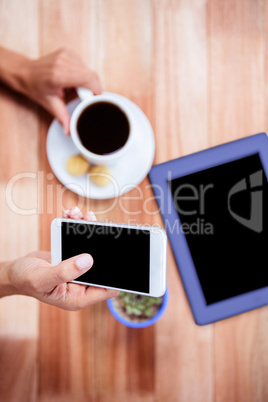 Overhead of feminine hands holding smartphone and coffee