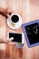 Overhead of feminine hands holding smartphone and coffee