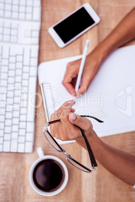 Businesswoman writing and holding eye glasses
