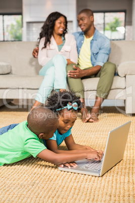 Happy siblings lying on the floor using laptop