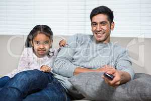 Smiling father watching tv with daughter on the sofa
