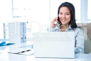 Smiling businesswoman phoning at the desk