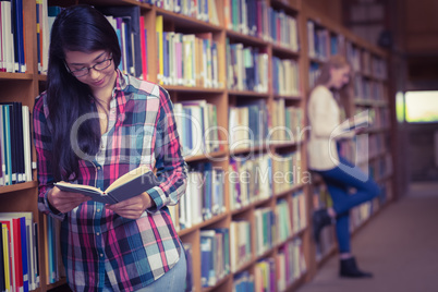 Smiling student leaning against bookshelves reading book