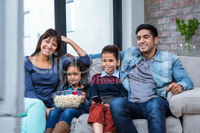 Happy young family eating popcorn while watching tv