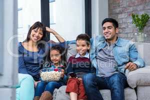 Happy young family eating popcorn while watching tv