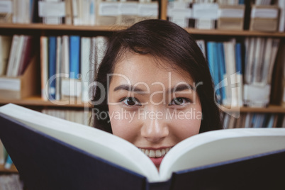 Smiling student hiding face behind a book