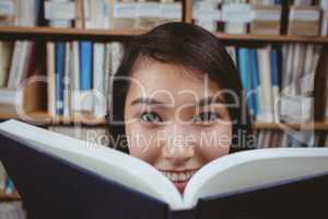 Smiling student hiding face behind a book