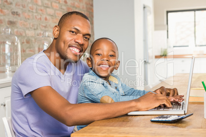 Cute son using laptop at desk with father