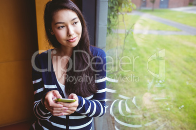 Smiling student with smartphone and looking through the window