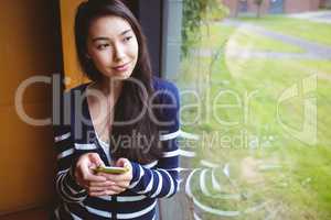 Smiling student with smartphone and looking through the window