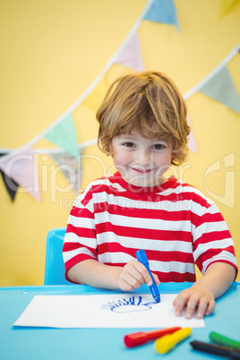 Smiling boy colouring some paper