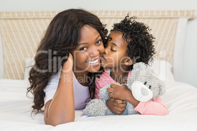 Young girl kissing her smiling mother on bed