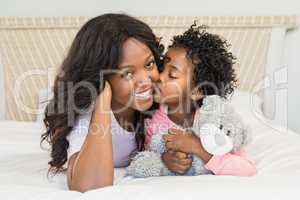 Young girl kissing her smiling mother on bed