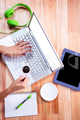 Overhead of feminine hands using laptop and holding coffee