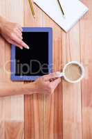 Overhead of feminine hands using tablet and holding coffee