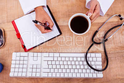 Doctor holding coffee cup and writing on diary