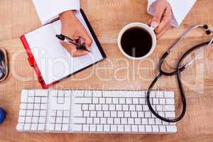 Doctor holding coffee cup and writing on diary