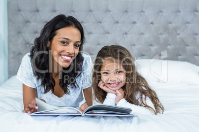 Happy mother and daughter reading a book on the bed