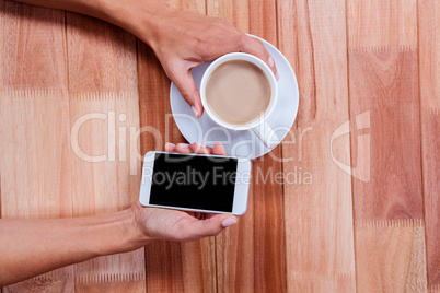 Hands holding smartphone and coffee